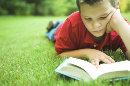 A little boy that is sitting in the grass reading