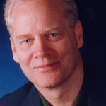 Andrew Clements wearing a suit and tie smiling at the camera