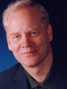 Andrew Clements wearing a suit and tie smiling at the camera