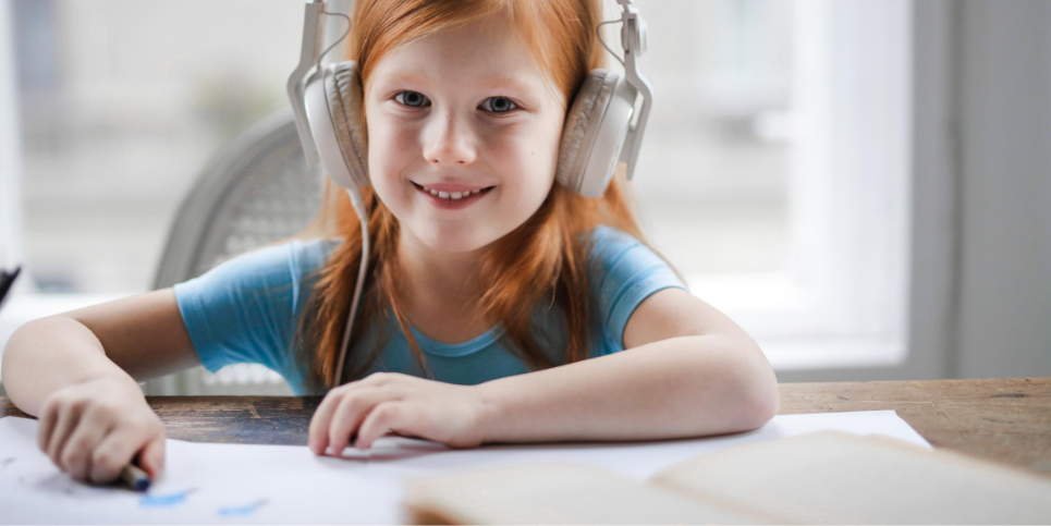 A little girl with headphones sitting at a table using a laptop