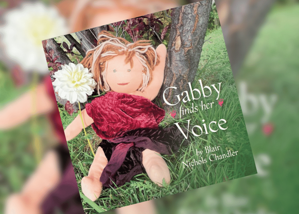 Gabby Finds Her Voice Header | The Children's Book Review Book cover for 'Gabby finds her Voice' showing a doll in a grassy garden with a white flower beside it.